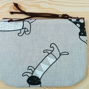 May include: A small, grey zippered pouch with a brown zipper pull. The pouch has a white and black print of stylised dogs on it.