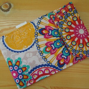 May include: A small fabric wallet with a colorful mandala pattern in shades of pink, blue, yellow, and white. The wallet has a flap closure and a white label.