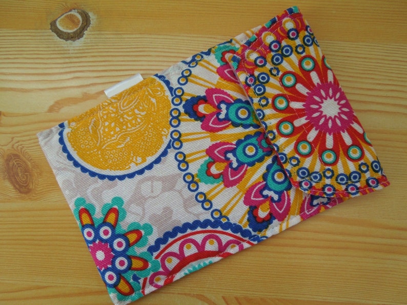 May include: A small fabric wallet with a colorful mandala pattern in shades of pink, blue, yellow, and white. The wallet has a flap closure and a white label.