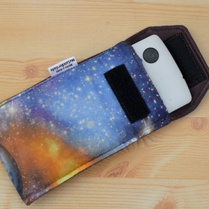 May include: A galaxy print phone case with a black strap and a white phone inside. The case has a label that reads "Made in South Africa".
