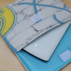 K&ouml;nnte beinhalten: Ein wei&szlig;es Tablet-Computer mit einer blauen und wei&szlig;en Stoffh&uuml;lle. Die H&uuml;lle hat ein Ziegelmuster und ein blaues Futter. Das Tablet hat das LG-Logo und die CE-Kennzeichnung.