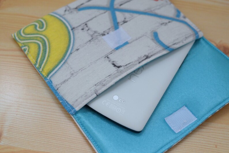 K&ouml;nnte beinhalten: Ein wei&szlig;es Tablet-Computer mit einer blauen und wei&szlig;en Stoffh&uuml;lle. Die H&uuml;lle hat ein Ziegelmuster und ein blaues Futter. Das Tablet hat das LG-Logo und die CE-Kennzeichnung.