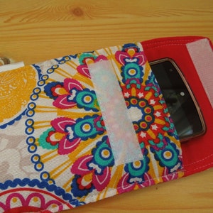 May include: A colorful phone case with a mandala pattern and a red flap with velcro closure. The case has a clear plastic window to view the phone screen.