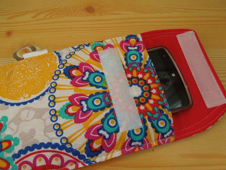 May include: A colorful phone case with a mandala pattern and a red flap with velcro closure. The case has a clear plastic window to view the phone screen.