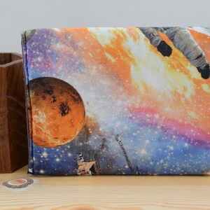 May include: A colorful zippered pouch with a space-themed design featuring an astronaut, a planet, and stars. The pouch has a black zipper and a white label with the text "www.etsy.com/shop/misterwobbly".