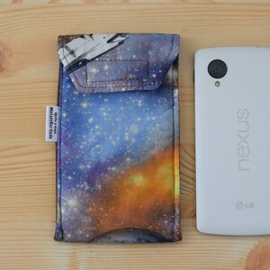 May include: A galaxy-themed phone case with a blue, purple, and orange design. The case has a flap that covers the top of the phone. The case is next to a white Nexus phone.