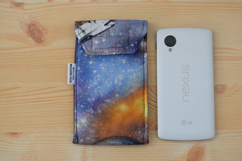May include: A galaxy-themed phone case with a blue, purple, and orange design. The case has a flap that covers the top of the phone. The case is next to a white Nexus phone.