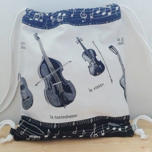 Puede incluir: Bolsa de cordón blanco con un diseño de notas musicales en negro y azul. La bolsa presenta ilustraciones de un violín, una guitarra y un contrabajo con las palabras francesas "le violon", "la guitare" y "la contrebasse".