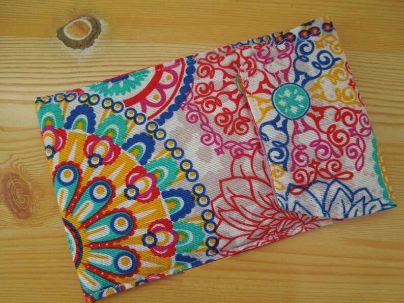May include: A colorful fabric pouch with a paisley pattern in shades of red, blue, yellow, and green. The pouch has a flap closure and is made of a soft, textured fabric.