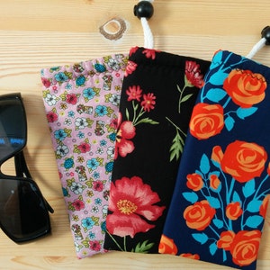 May include: Three different patterned fabric pouches for sunglasses. The pouches are made of cotton and have a drawstring closure. The pouches are in pink, black, and blue with floral patterns.