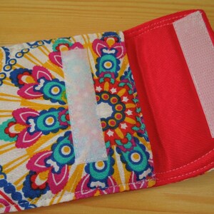 May include: A small, red fabric pouch with a white velcro closure. The pouch has a colorful paisley pattern on the front.