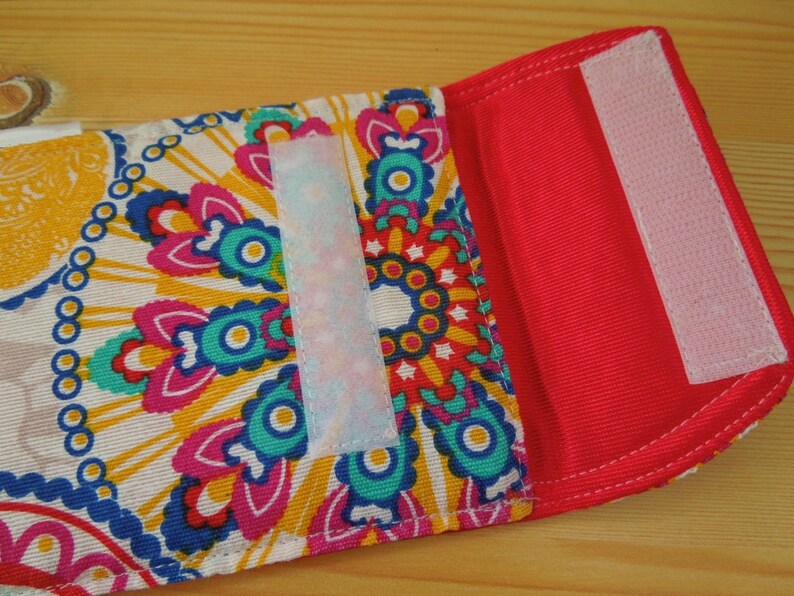 May include: A small, red fabric pouch with a white velcro closure. The pouch has a colorful paisley pattern on the front.