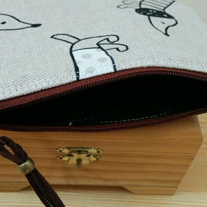 May include: A beige zippered pouch with a brown zipper and a brown tassel. The pouch has a black and white print of dogs on it.
