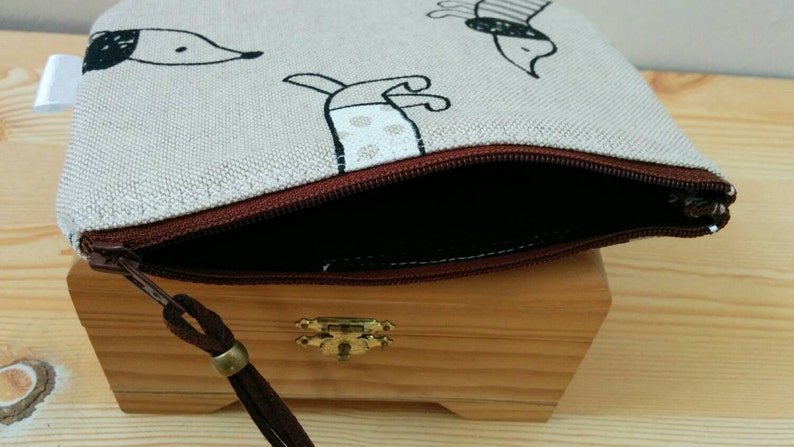 May include: A beige zippered pouch with a brown zipper and a brown tassel. The pouch has a black and white print of dogs on it.