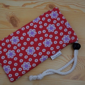 May include: Red drawstring bag with a white and purple floral pattern. The bag has a white drawstring and a black toggle.