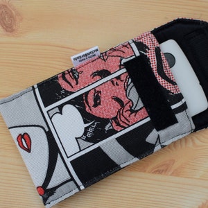 Pu&ograve; includere: Una custodia per telefono in bianco e nero con un design in stile fumetto che presenta una donna con labbra rosse e un fumetto che dice "B-R-I-L-L". La custodia ha una patta nera con chiusura a velcro.