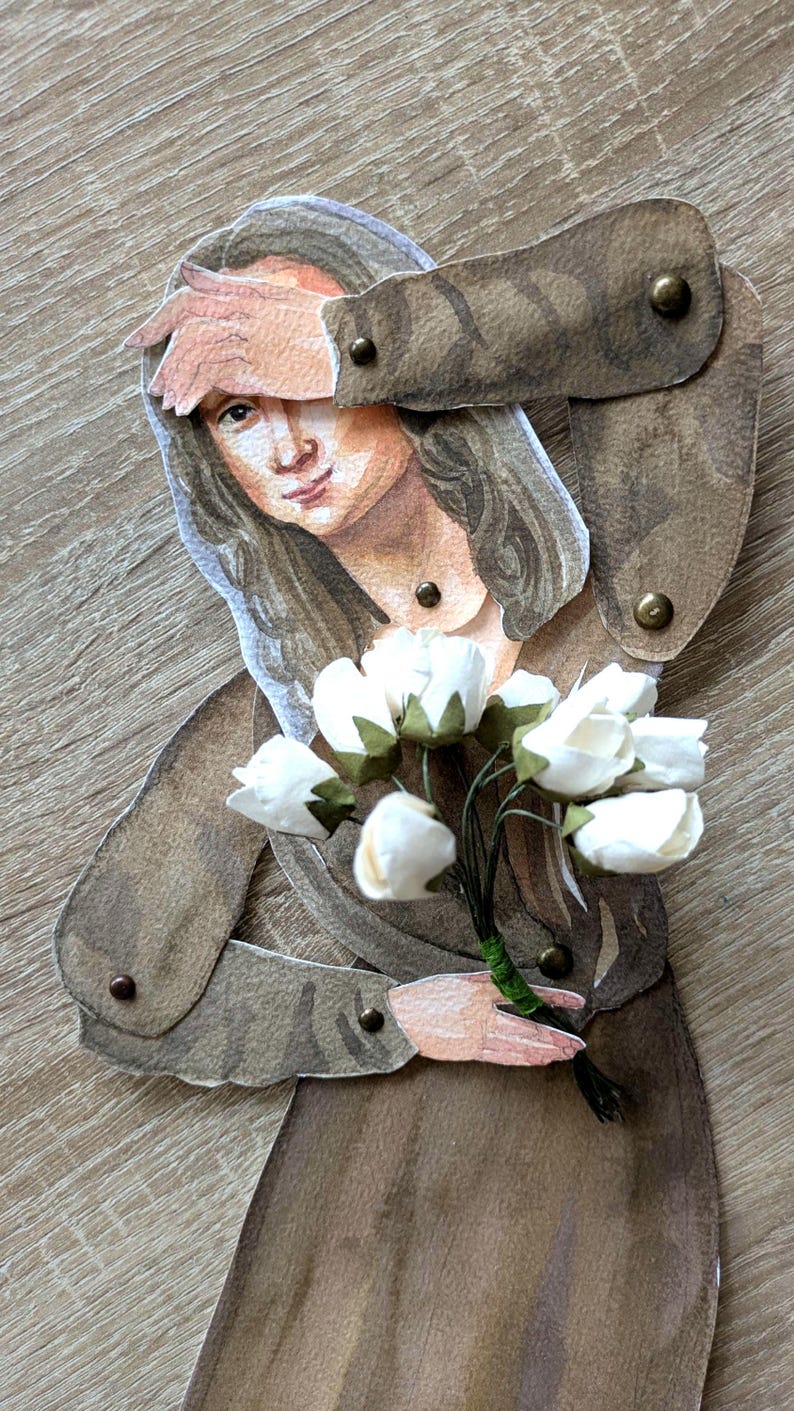 May include: A paper cutout of a woman in a brown dress, holding a bouquet of white flowers. The woman's arm is raised to her forehead. The cutout is attached with small brass rivets. The background is a light brown wood grain.