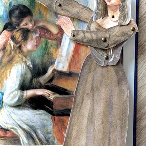 May include: A pop-up book featuring a paper cutout of the Mona Lisa with articulated arms and legs. The background shows a painting of women around a piano. The cutout is wearing a brown dress and jacket.