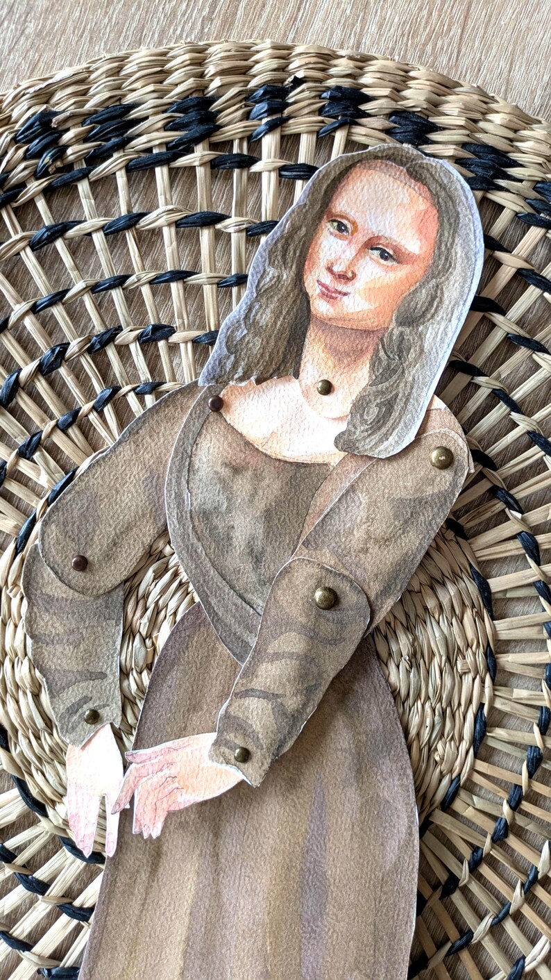May include: A paper cutout of the Mona Lisa, with articulated arms, is positioned over a woven basket. The artwork features a brown dress and long, wavy hair. The basket has a circular design with natural and black woven elements.