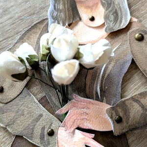 May include: A paper cutout of the Mona Lisa holding a bouquet of white flowers. The artwork is in shades of brown, beige, and cream. The figure's hair is long and wavy, and the hands are delicately posed.