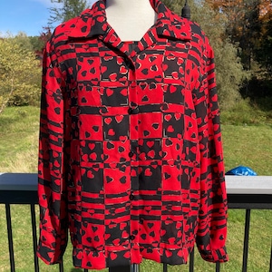 May include: A red and black button-up shirt with a geometric pattern of hearts. The shirt has a collar and long sleeves.