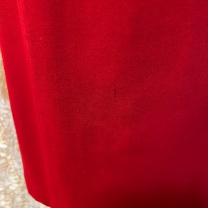 Puede incluir: Primer plano de una tela roja lisa, posiblemente ropa. La tela tiene un aspecto texturizado y un ligero brillo. El borde inferior de la tela es visible, con una sutil curva. Hay una peque&ntilde;a mancha oscura en la tela.