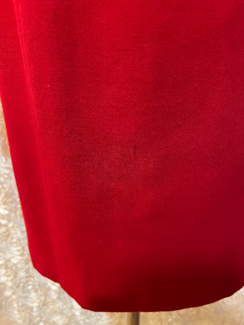 Puede incluir: Primer plano de una tela roja lisa, posiblemente ropa. La tela tiene un aspecto texturizado y un ligero brillo. El borde inferior de la tela es visible, con una sutil curva. Hay una peque&ntilde;a mancha oscura en la tela.
