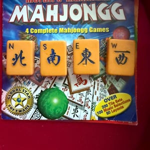 May include: A Mahjongg game set with the title "Moraff's Maximum Mahjongg" on the box. The game includes four yellow tiles with blue characters, a green ball, and a "Global Star Software" logo. The box also states "4 Complete Mahjongg Games".
