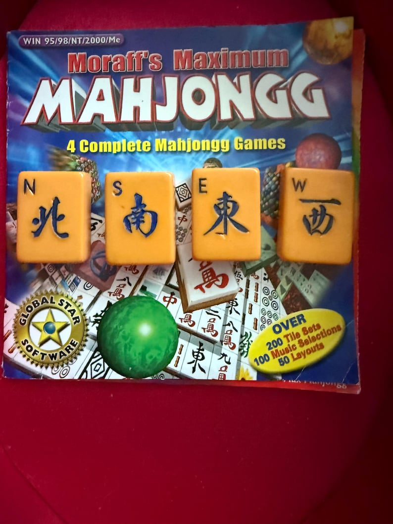May include: A Mahjongg game set with the title "Moraff's Maximum Mahjongg" on the box. The game includes four yellow tiles with blue characters, a green ball, and a "Global Star Software" logo. The box also states "4 Complete Mahjongg Games".
