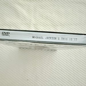 May include: A sealed DVD case for Michael Jackson's This Is It. The spine is white with black text reading DVD and Michael Jackson's This Is It. The case is wrapped in clear plastic film, showing the side profile of the rectangular media product.
