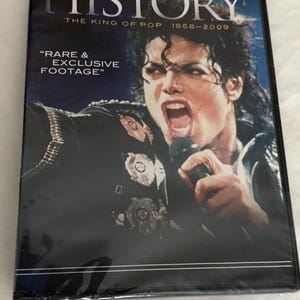 May include: A DVD case featuring Michael Jackson on the cover with the text "HISTORY THE KING OF POP 1958-2009" and "RARE & EXCLUSIVE FOOTAGE". The image shows Michael Jackson singing into a microphone while wearing a black jacket with metallic emblems.