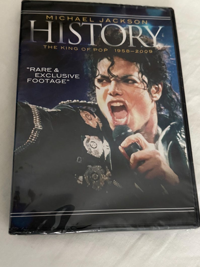 May include: A DVD case featuring Michael Jackson on the cover with the text "HISTORY THE KING OF POP 1958-2009" and "RARE & EXCLUSIVE FOOTAGE". The image shows Michael Jackson singing into a microphone while wearing a black jacket with metallic emblems.
