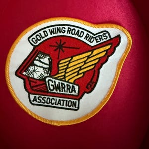 May include: A red patch with a white border featuring the text "GOLD WING ROAD RIDERS" and "GWRRA ASSOCIATION". The patch has a red and yellow wing design and a starburst.