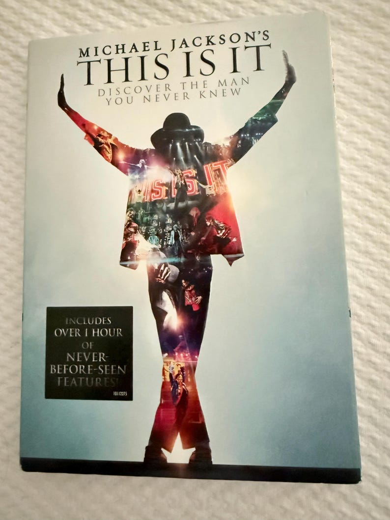 May include: A DVD case for Michael Jackson's This Is It, featuring a silhouette of the performer with arms raised. The cover includes the text "Michael Jackson's This Is It, Discover the Man You Never Knew" and a black box stating "Includes over 1 hour of never-before-seen features!"