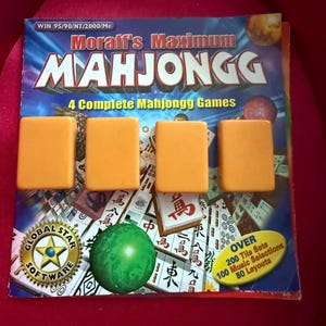 May include: A Mahjongg game set with four orange tiles in front of the game box. The box has the title "Moraff's Maximum Mahjongg" and includes the text "4 Complete Mahjongg Games". A green sphere and a Global Star Software logo are also visible.
