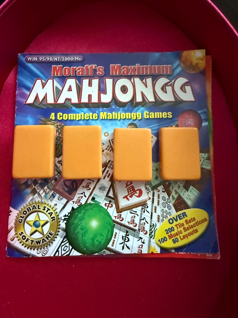 May include: A Mahjongg game set with four orange tiles in front of the game box. The box has the title "Moraff's Maximum Mahjongg" and includes the text "4 Complete Mahjongg Games". A green sphere and a Global Star Software logo are also visible.