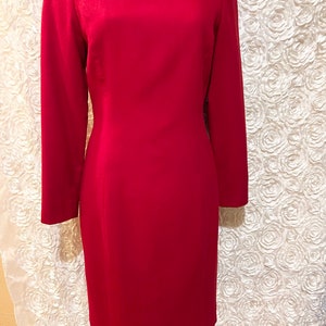 Puede incluir: Un vestido rojo vibrante con mangas largas y una silueta cl&aacute;sica. El vestido presenta un cuello redondo y est&aacute; adornado con botones dorados en el hombro. El vestido se exhibe en un maniqu&iacute;.