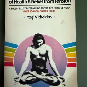May include: A book cover titled "The Yoga System of Health & Relief from Tension." It features a man in a seated yoga pose within a pink circle, with a rainbow-colored stripe above. The text includes "A Fully-Illustrated Guide" and the author's name.