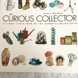 May include: A book cover titled "The Curious Collector" by Jessie Walker, featuring a collection of vintage items. The items include a coffee pot, figurines, watering cans, teacups, and a decorative vase. The book cover is white.
