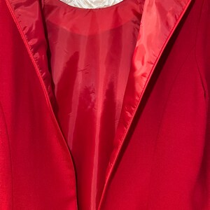 Puede incluir: Un blazer rojo con dise&ntilde;o de cuello en V, colgado de una percha rosa. El forro interior es de un tono rojo m&aacute;s claro. El blazer es de la marca Brooks Brothers.