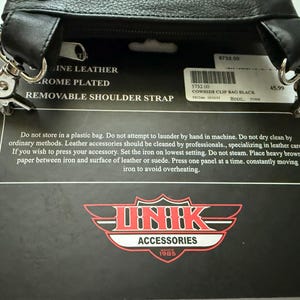 May include: A black cowhide leather clip bag with chrome-plated hardware and a removable shoulder strap. The product packaging includes care instructions and the Unik Accessories logo. The label reads: COWHIDE CLIP BAG BLACK 5732.00.