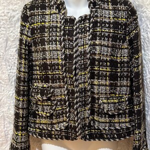 May include: A brown, black, and yellow tweed jacket with two front pockets and a white trim. The jacket is displayed on a mannequin and has a classic, tailored design. The fabric has a woven texture.