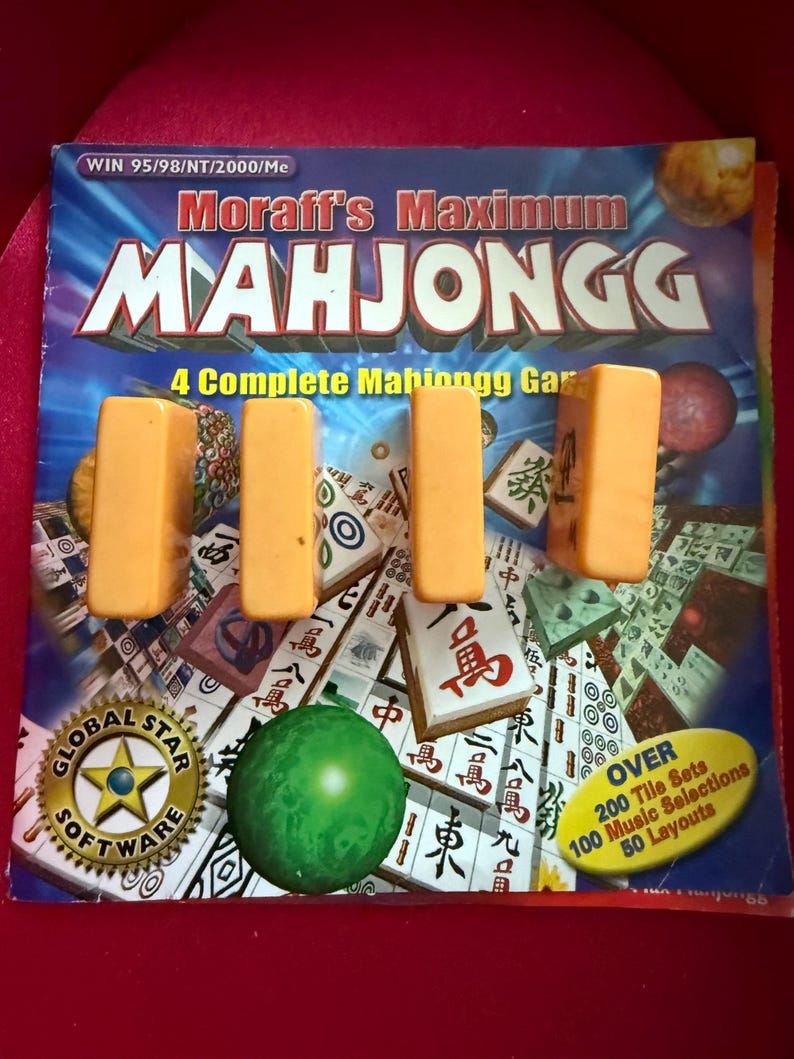May include: A Mahjongg game set with orange tiles and a green sphere. The game box features the text "Moraff's Maximum Mahjongg" and "4 Complete Mahjongg Games". The box also has the Global Star Software logo and details about tile sets and music selections.