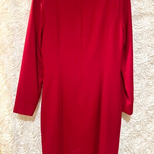 Puede incluir: Vestido rojo de manga larga, hasta la rodilla. El vestido tiene un corte entallado con cremallera trasera y una peque&ntilde;a abertura en el dobladillo. La tela parece ser de color liso, adecuado para ocasiones formales.