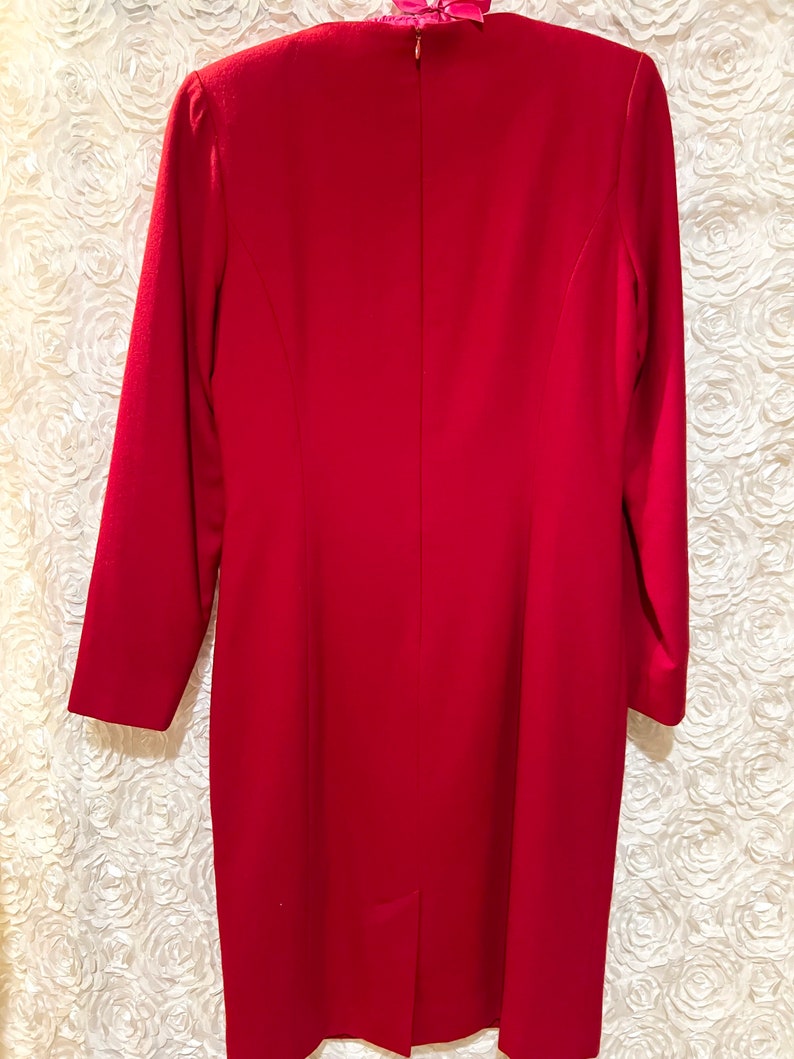 Puede incluir: Vestido rojo de manga larga, hasta la rodilla. El vestido tiene un corte entallado con cremallera trasera y una peque&ntilde;a abertura en el dobladillo. La tela parece ser de color liso, adecuado para ocasiones formales.