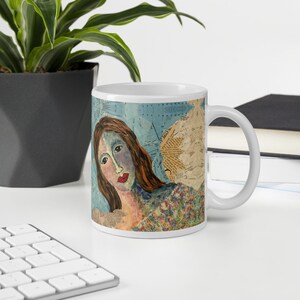 Może przedstawiać: Biały kubek ceramiczny z kolorowym wzorem kolażu przedstawiającym twarz kobiety i tło w postaci mapy. Kobieta ma niebiesko-zieloną sk&oacute;rę, brązowe włosy i czerwone usta.