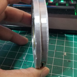 May include: A silver-colored, round, 3D printed object with a textured surface. The object has a small, black, rectangular opening on the side.
