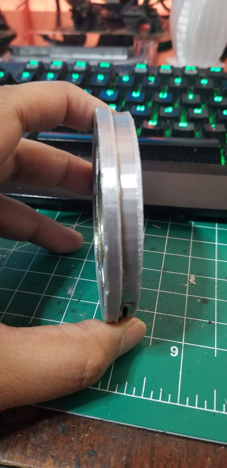 May include: A silver-colored, round, 3D printed object with a textured surface. The object has a small, black, rectangular opening on the side.