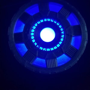 May include: A blue and black 3D printed replica of the Iron Man Arc Reactor. The reactor is lit up with a bright blue light.