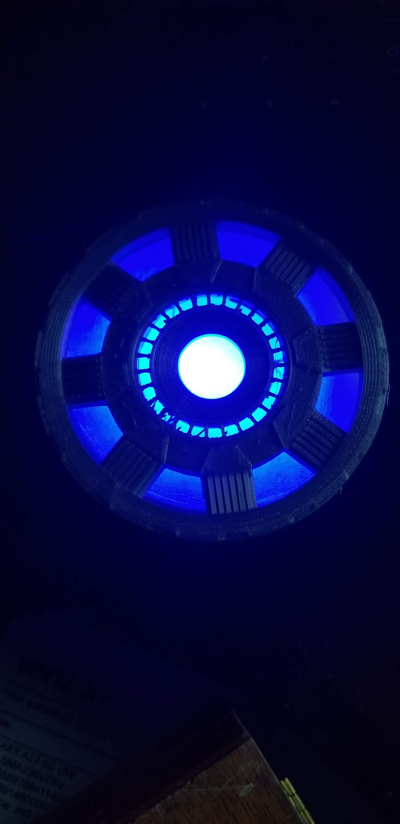 May include: A blue and black 3D printed replica of the Iron Man Arc Reactor. The reactor is lit up with a bright blue light.